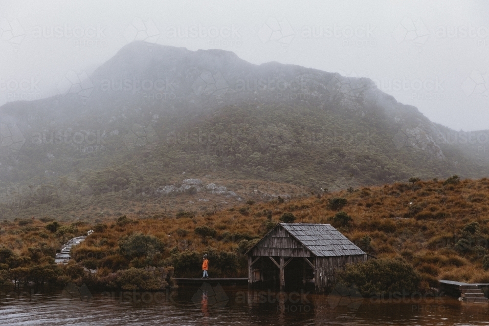 Child beside boat shed with mountain in background - Australian Stock Image