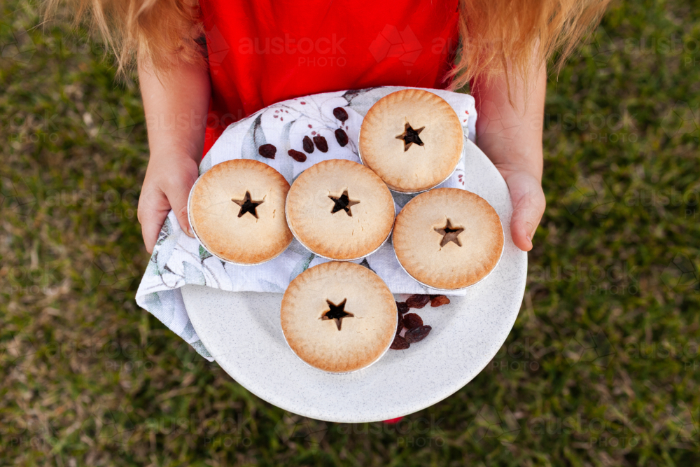 Child carrying plate of fruit mince pies to share outside in backyard at Christmas   - Australian Stock Image