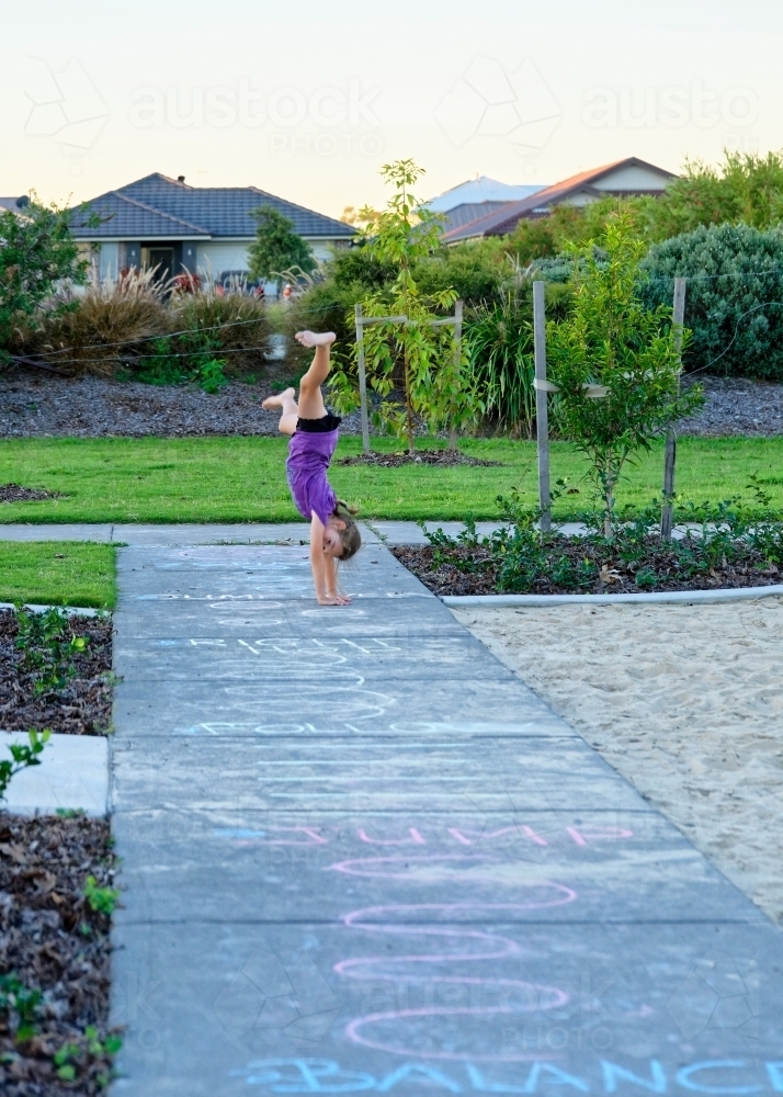 Child doing cartwheels in the park following chalk drawing on the pavement - Australian Stock Image
