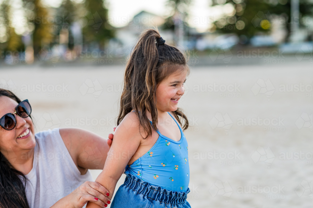 Child enjoys time at beach with adult who is assisting her while laughing under soft evening light. - Australian Stock Image
