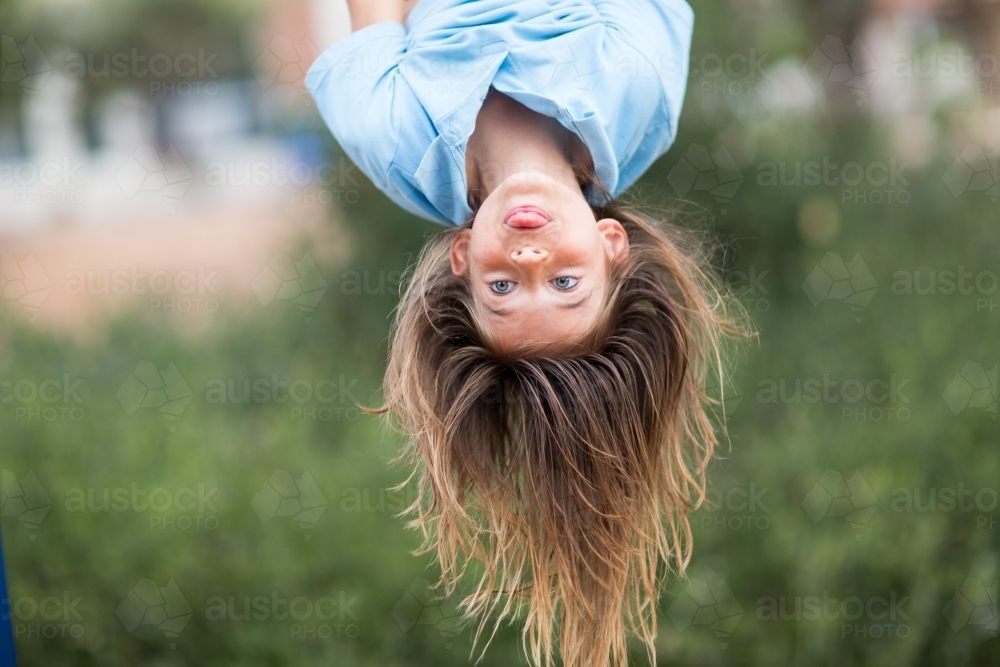 Child hanging upside downing poking tongue - Australian Stock Image