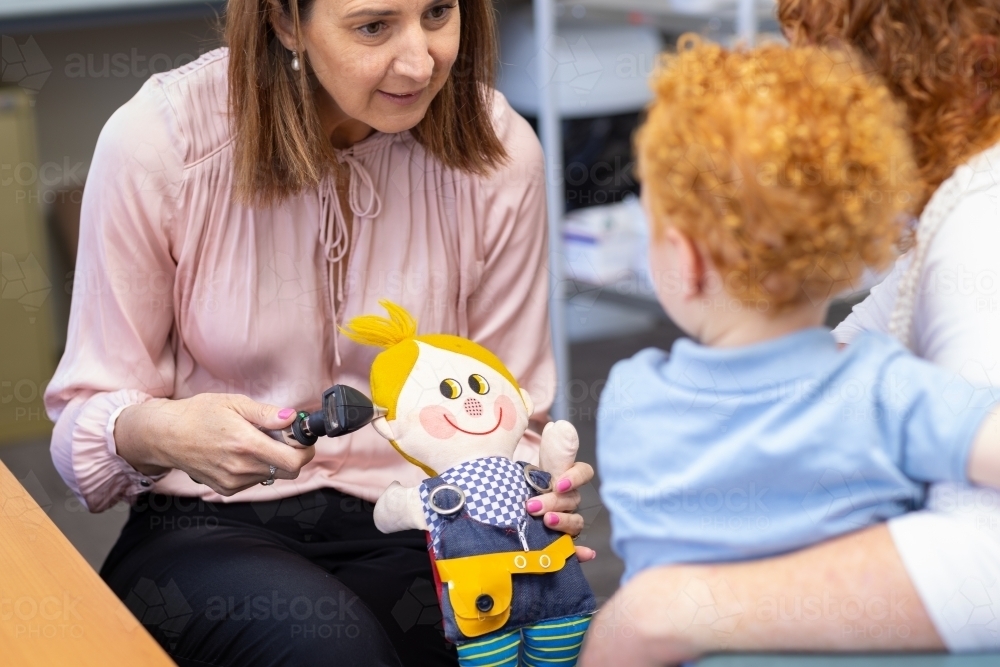 child health nurse demonstrating otoscope on toy to little boy - Australian Stock Image