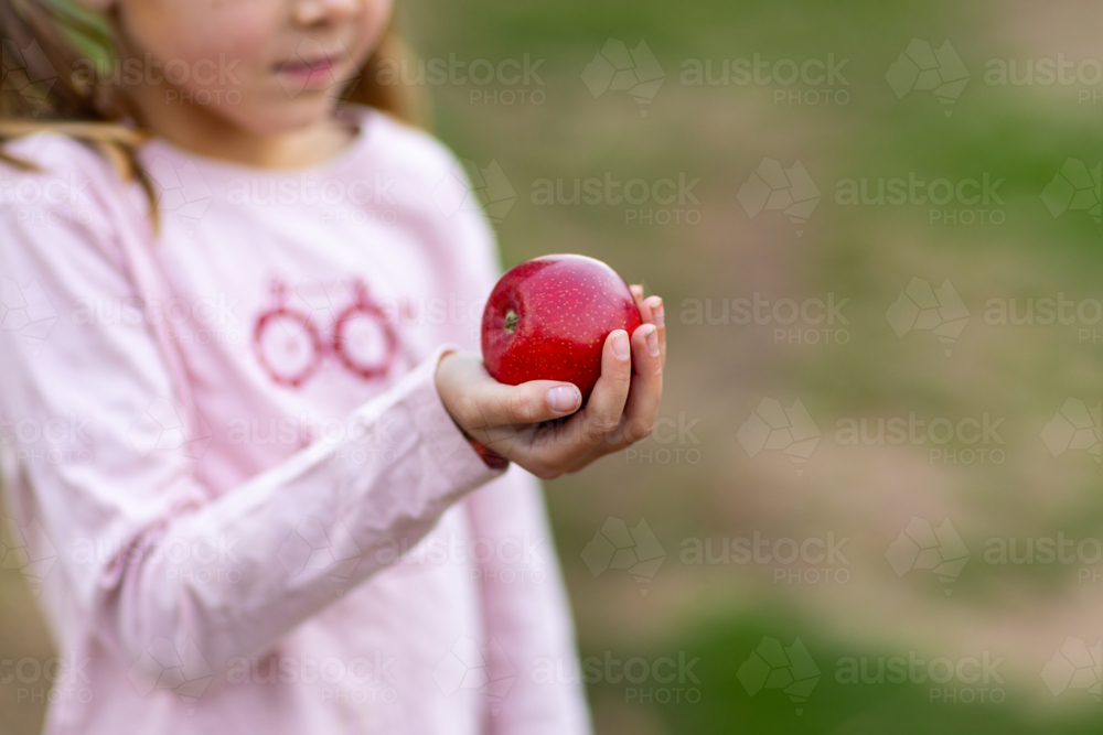 child holding shiny red apple in one grubby hand - Australian Stock Image