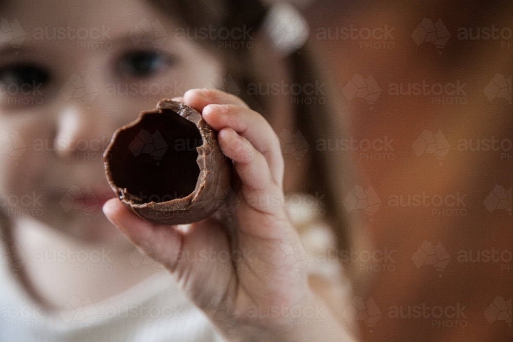 Child holding up hollow chocolate Easter egg she is eating - Australian Stock Image