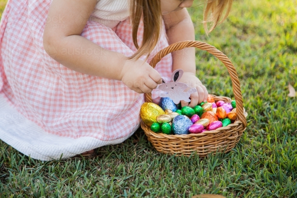 Child hunting for Easter eggs in garden on sunlit morning - Australian Stock Image