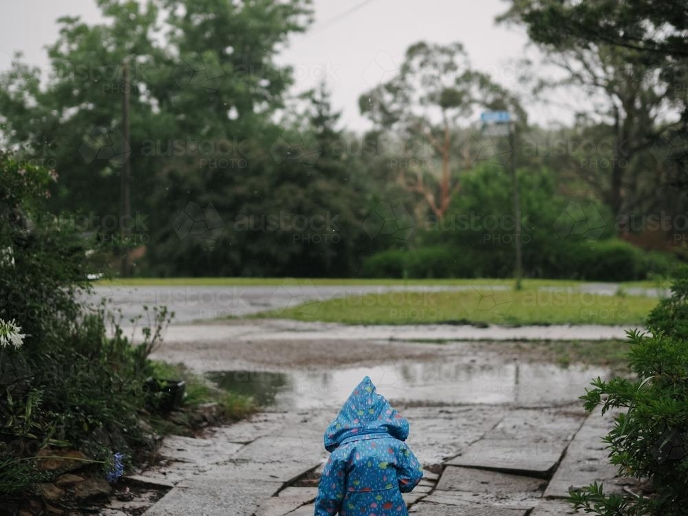 Child in blue raincoat walking out into the rain - Australian Stock Image