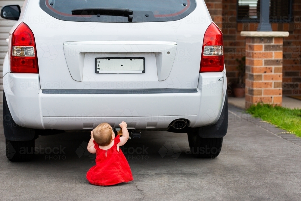 Image of Child in dangerous spot siting behind car in driveway ...