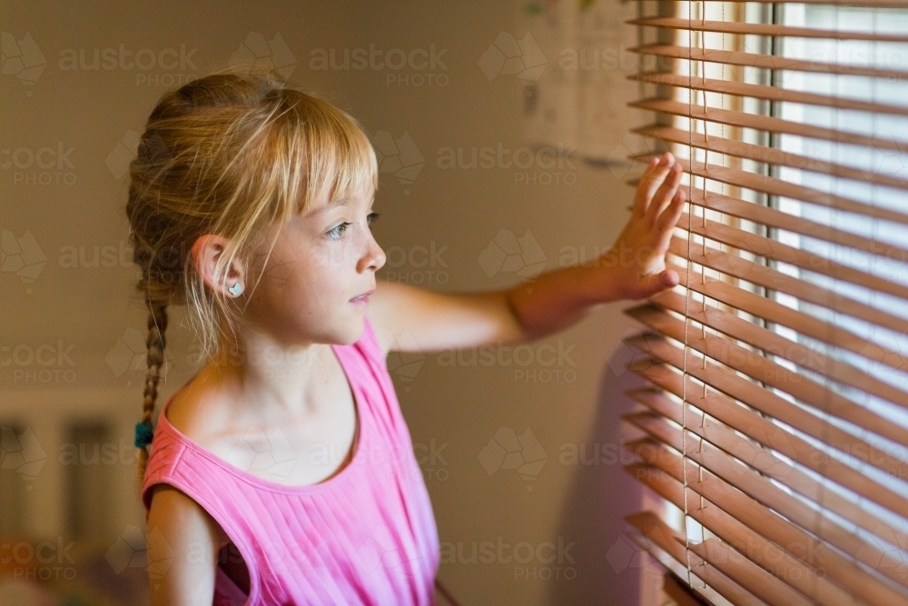 Child looking out through venetian blinds - Australian Stock Image