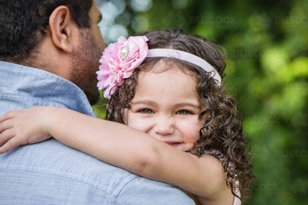 Child looking over Aboriginal father's shoulder smiling - Australian Stock Image