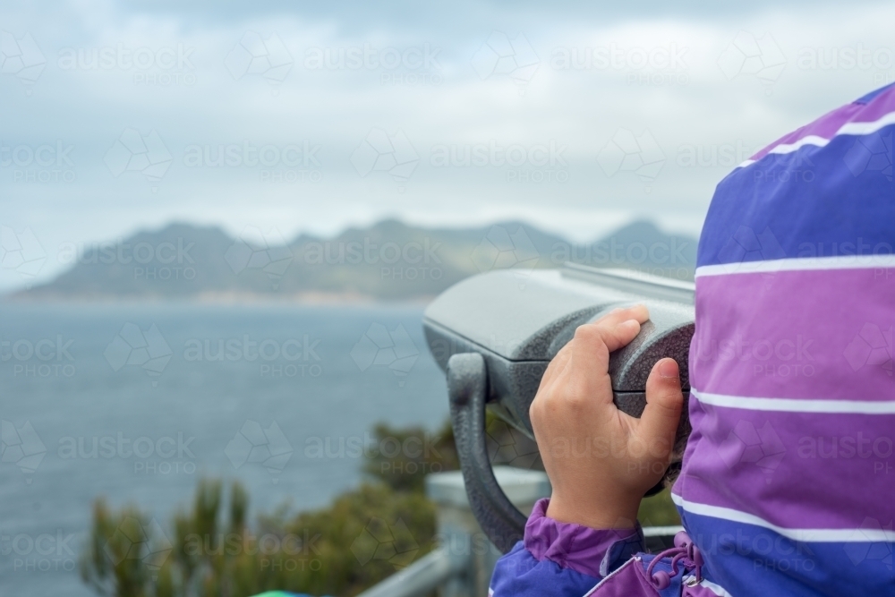 Child looking through binoculars at cliffs and ocean - Australian Stock Image