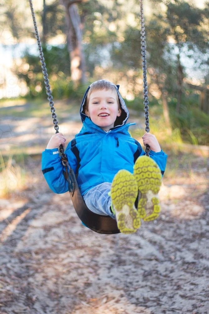 Child on a swing in a park on a winter morning - Australian Stock Image