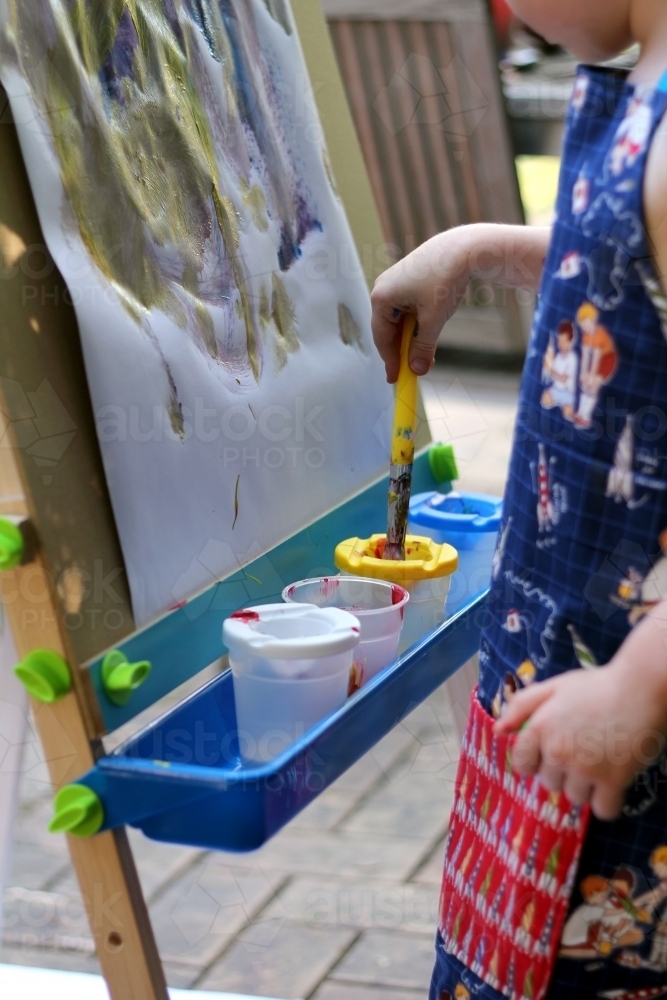 Child painting at easel - Australian Stock Image