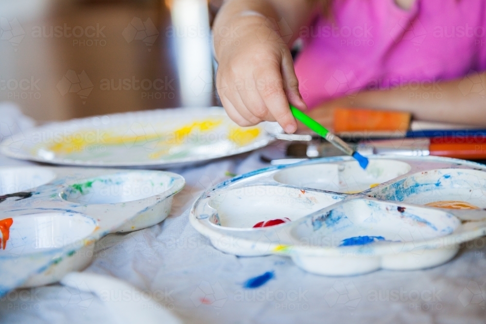 Child painting with paint brush and colourful paint - Australian Stock Image