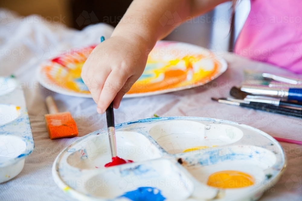 Child painting with paint brush and colourful paint - Australian Stock Image