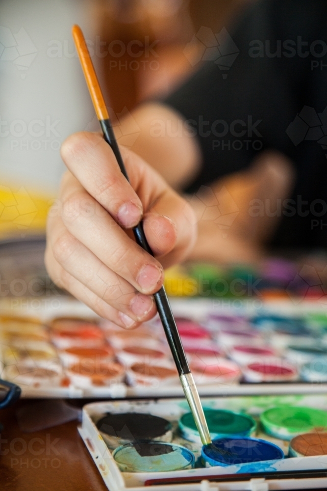 Child painting with watercolour paint and brush - Australian Stock Image