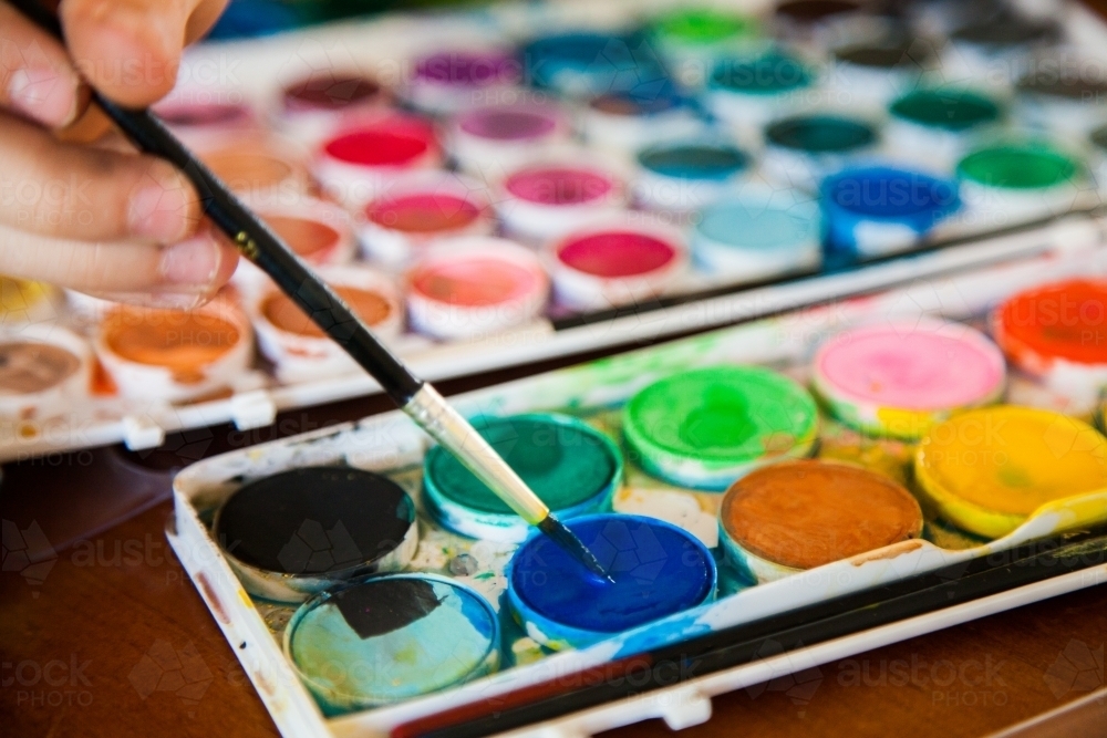 Child painting with watercolour paint and brush - Australian Stock Image