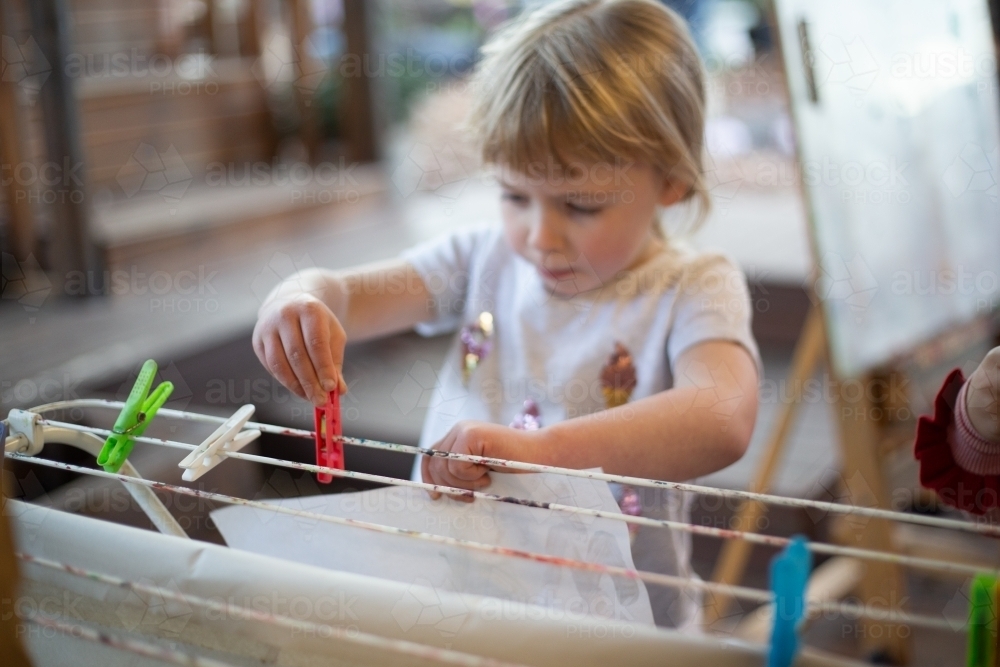 Child pegs a painting to dry at preschool - Australian Stock Image