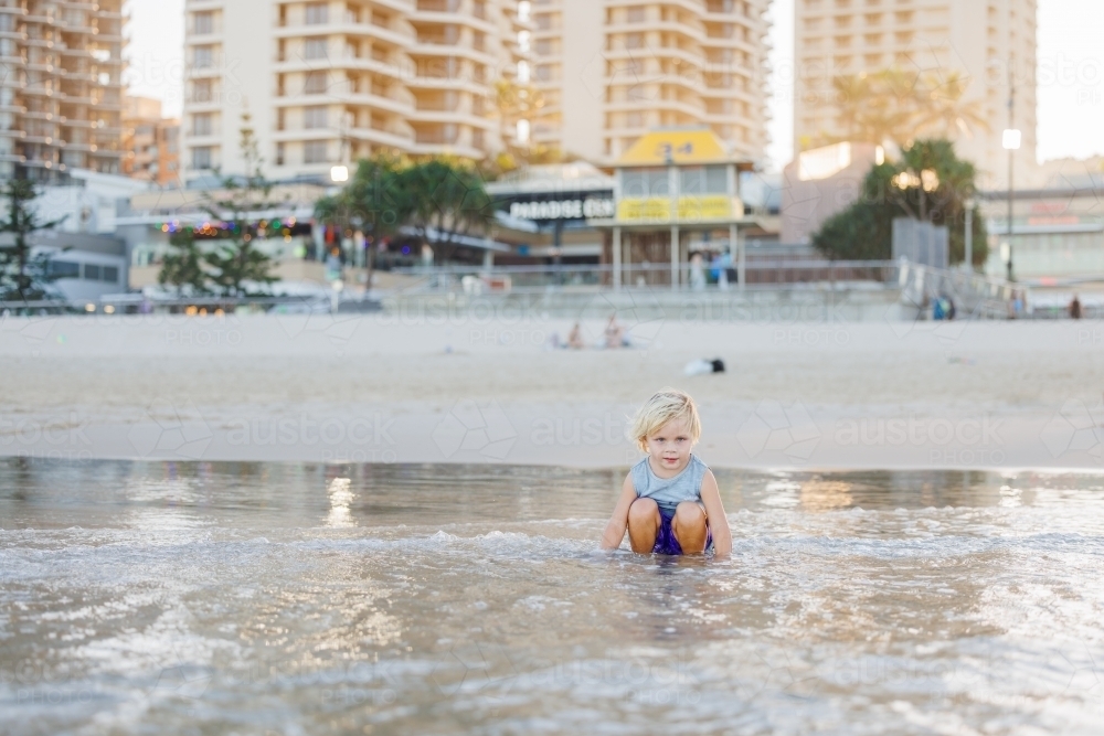 Child playing in shallow water on Gold Coast beach in golden afternoon light - Australian Stock Image