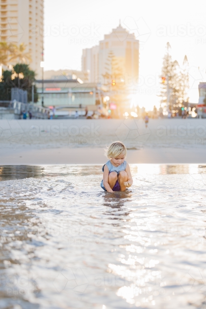 Child playing in shallow water on Gold Coast beach in golden afternoon light - Australian Stock Image