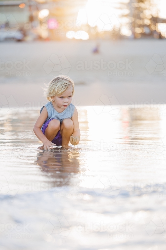 Child playing in shallow water on Gold Coast beach in golden afternoon light - Australian Stock Image