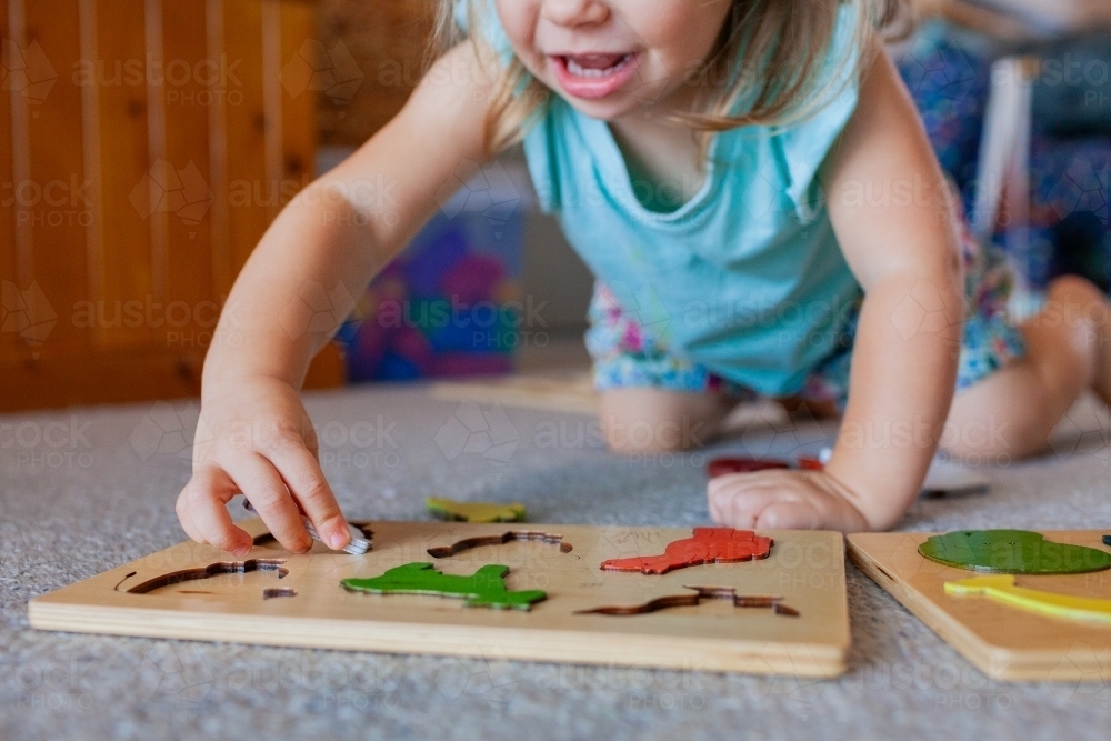 Child playing on floor fitting wooden animal puzzle pieces into board - Australian Stock Image
