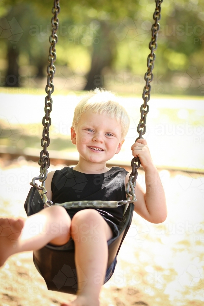 Child playing on swing at playground in Summer - Australian Stock Image