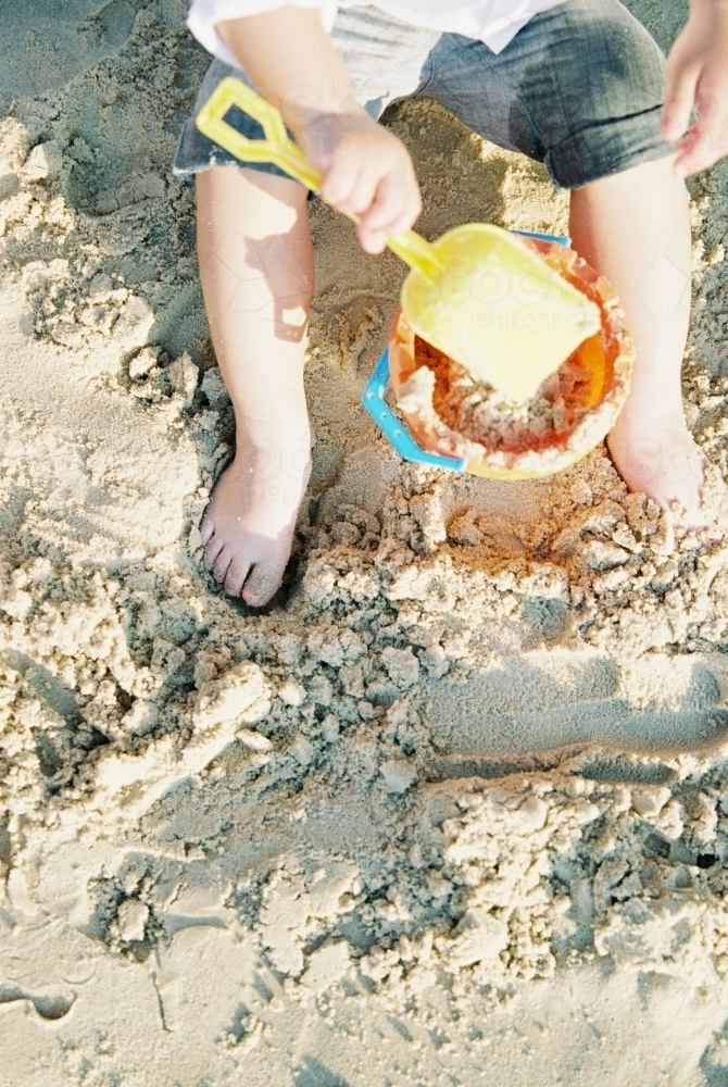 Child playing with bucket and spade in the sand at the beach - Australian Stock Image