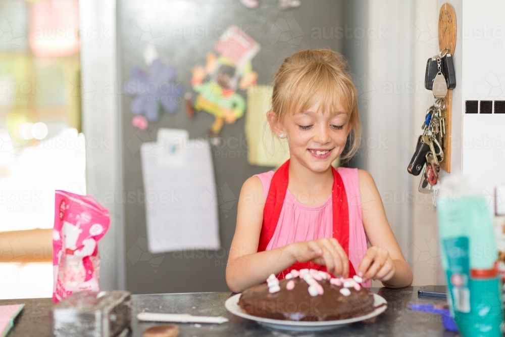 Child putting marshmallows on cake icing - Australian Stock Image
