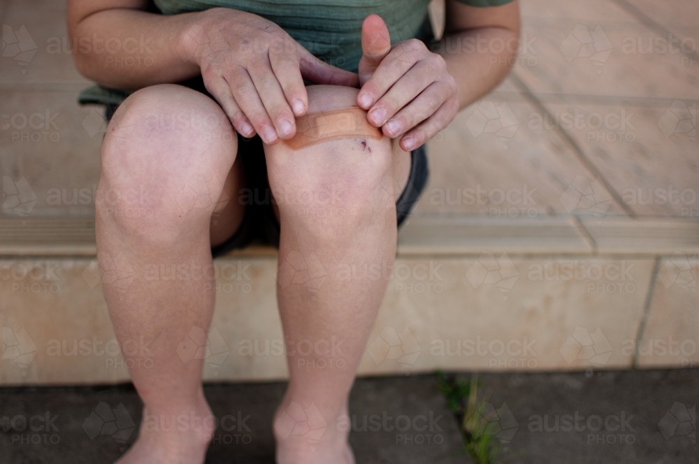 Child putting plaster on knee - Australian Stock Image
