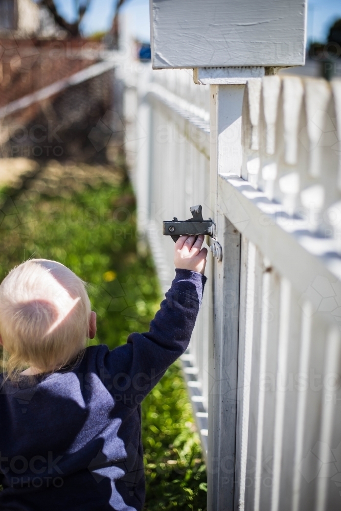 Child reaching up to open gate on white fence - Australian Stock Image