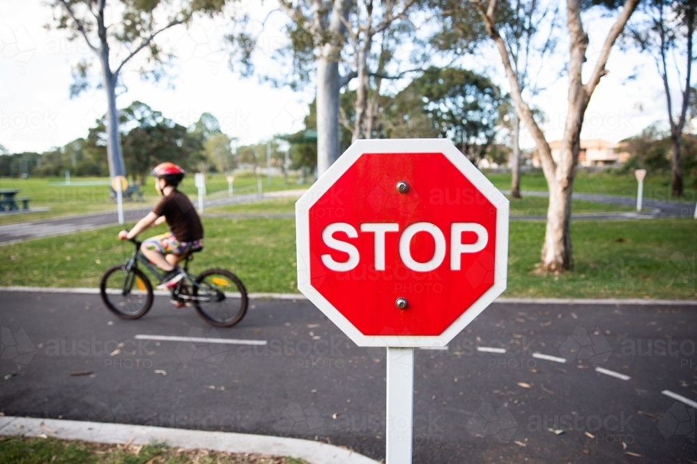 child riding past a stop sign on a bike track with road markings - Australian Stock Image