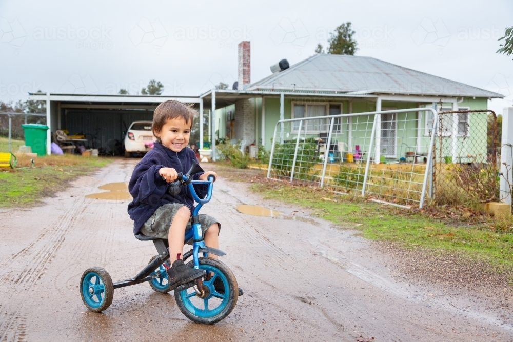 Child riding tricycle in puddles - Australian Stock Image