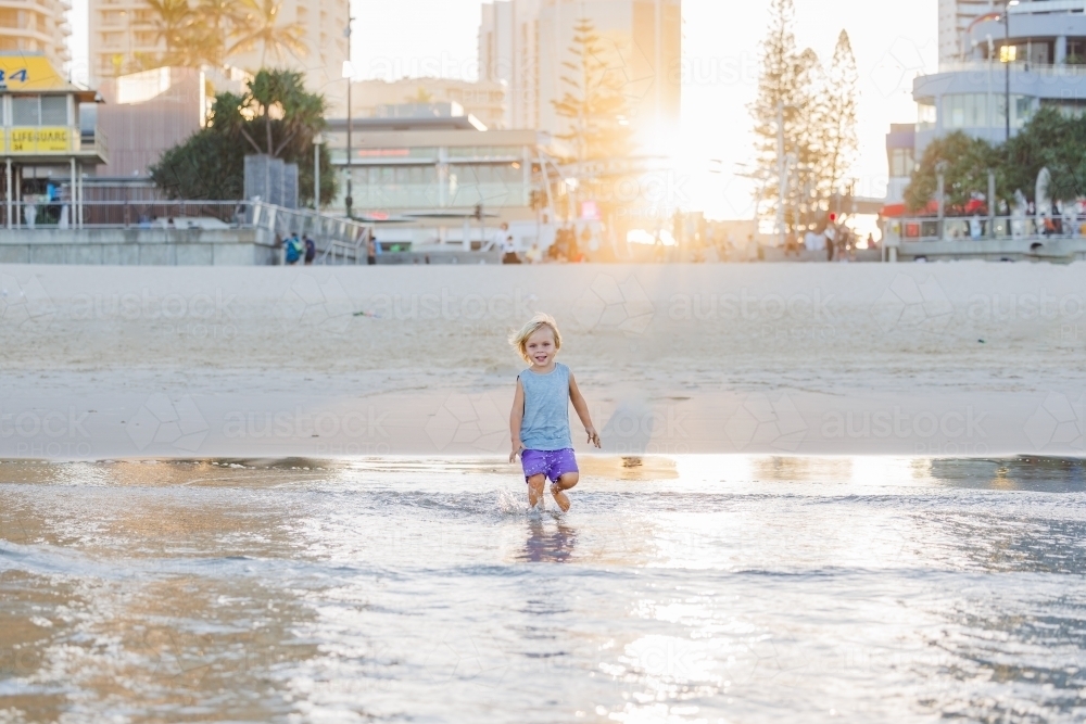 Child running in shallow water on Gold Coast beach at Surfers Paradise - Australian Stock Image