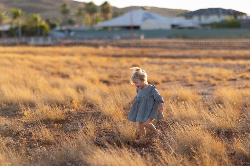 child running through dry grass with houses of town blurred in background - Australian Stock Image
