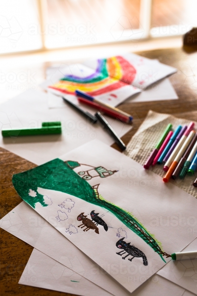 Child's drawing of sheep, dogs and a farm sitting on a table with textas and other art materials - Australian Stock Image