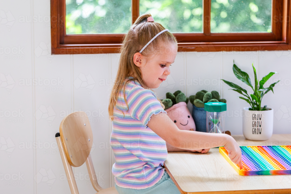 Child sitting at desk in speech pathology clinic concentrating on rainbow poppet toy - Australian Stock Image