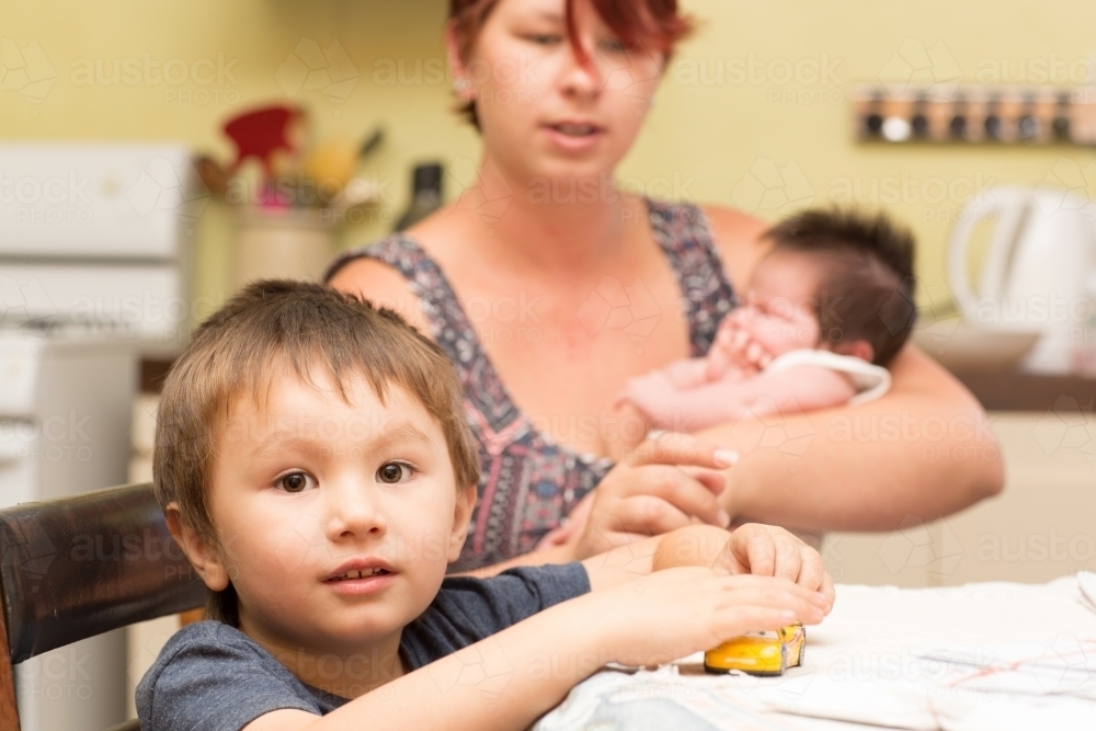 Child sitting at table with mother and baby behind - Australian Stock Image