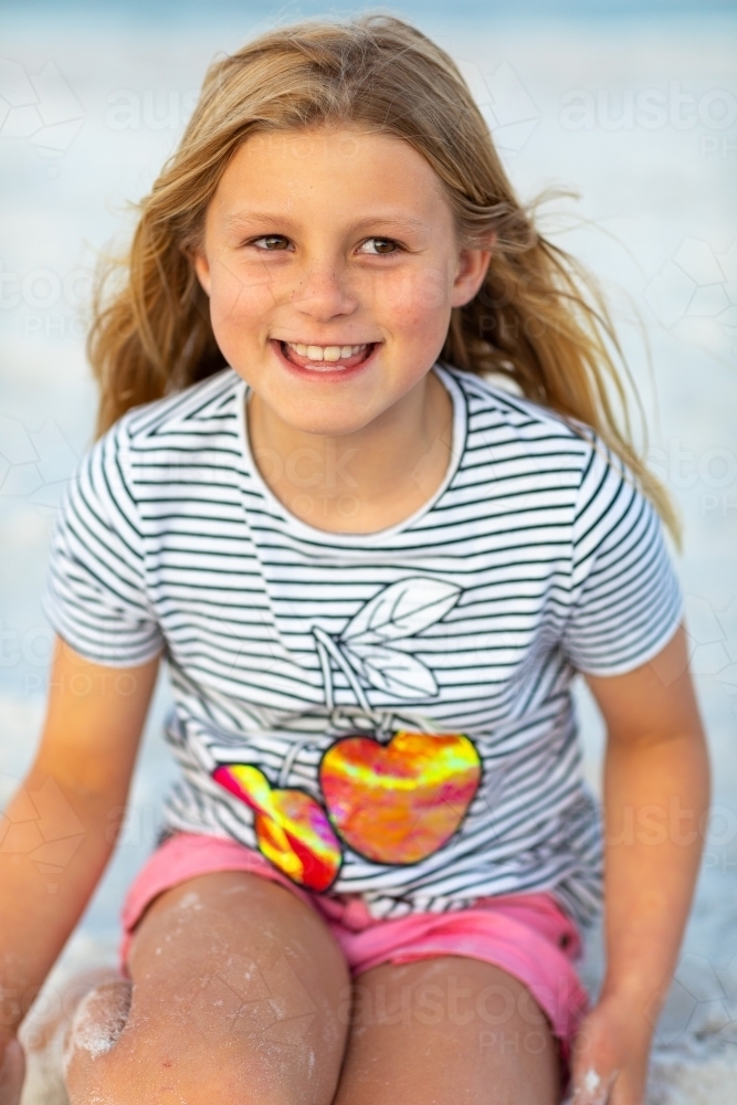 Child sitting on beach in striped tee-shirt - Australian Stock Image