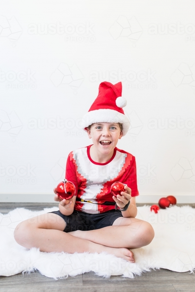 Child sitting on rug at Christmas time holding decorations excited - Australian Stock Image