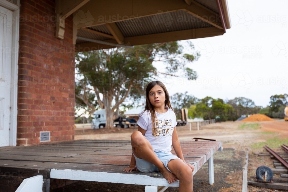 child sitting on siding verandah with truck and works behind - Australian Stock Image