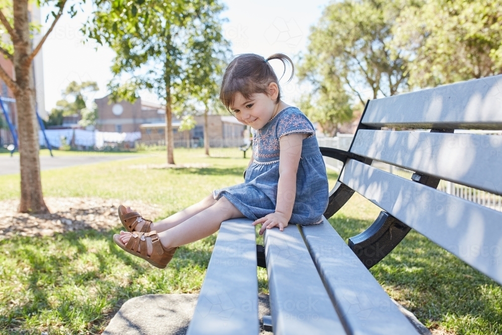 Child smiling on park bench wearing a blue dress - Australian Stock Image