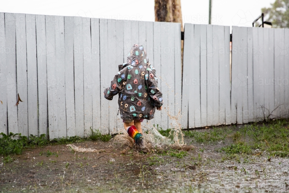 child splashing in puddles during a downpour - Australian Stock Image