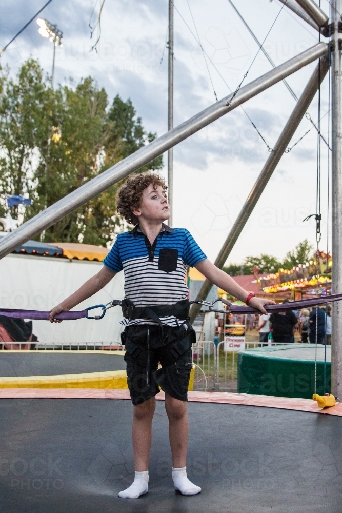 Child standing on trampoline at show strapped into harness - Australian Stock Image