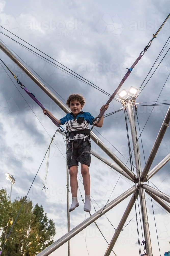 Child strapped into harness on ride at show jumping in air smiling - Australian Stock Image