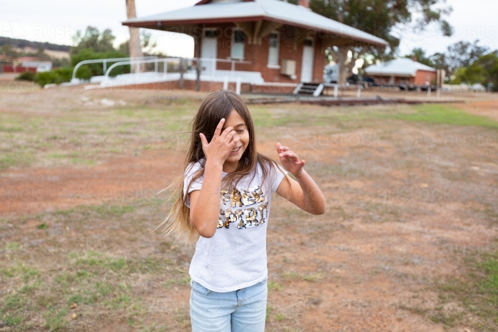 Child sweeping hair out of eyes in old railway yard - Australian Stock Image
