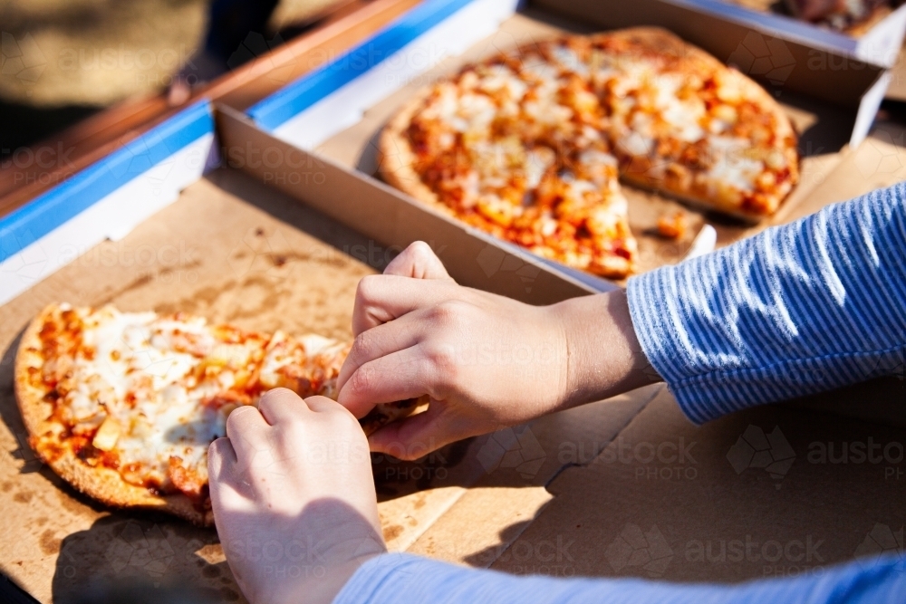 Child taking slice of takeaway pizza from box - Australian Stock Image