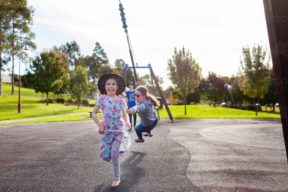 Child, teen and young adult siblings playing together on flying fox swing at playground - Australian Stock Image