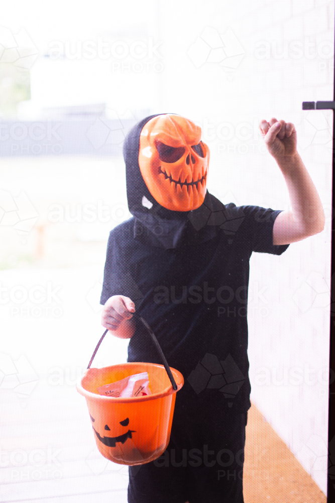 child trick or treating in a mask knocking on a door - Australian Stock Image