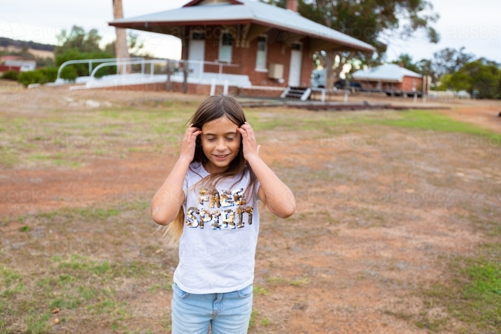 child tucking long hair behind her ears at old railway siding - Australian Stock Image
