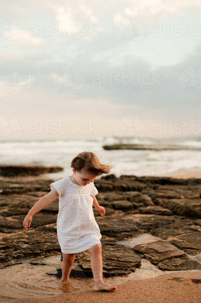 Child walking on rocks at sunset by the beach - Australian Stock Image